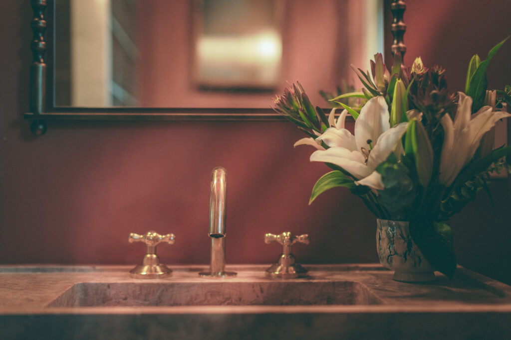 Handmade pink travertine sink with brass faucet and fresh white lilies in coral powder room. Interior design by Tenlie Mourning