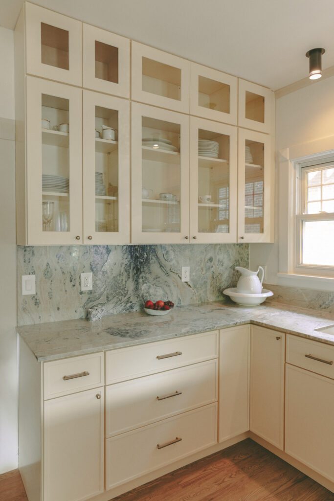Ivory kitchen with glass-front cabinetry quartzite countertops and brass shelving by Tenlie Mourning interior designer. Madison street project