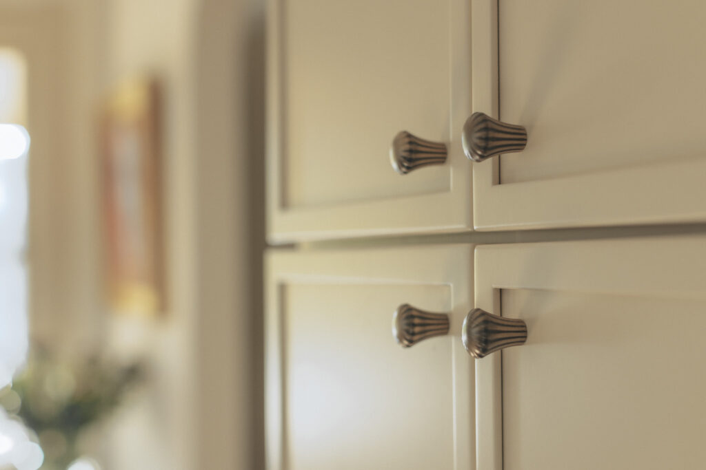Brass cabinet pulls on white slim- shaker style kitchen cabinetry detail shot. Interior design by Tenlie Mourning